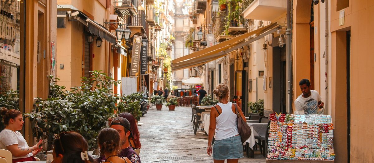 Une rue sicilienne avec les tables en terrasse et l’étal de souvenirs · grammaire italienne A1