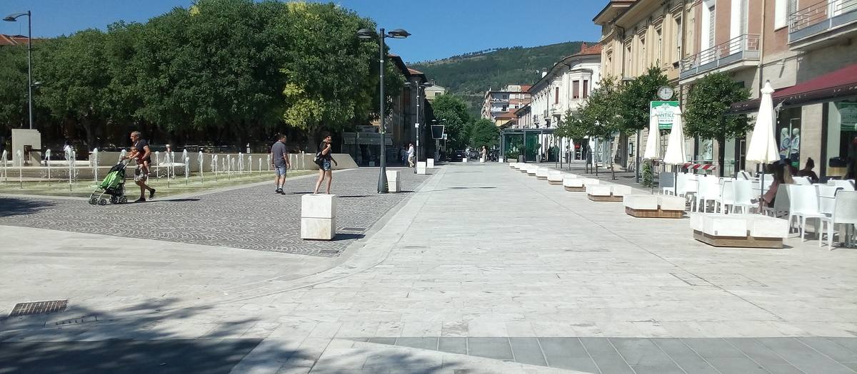 Una plaza peatonal con una fuente y mesas de bar