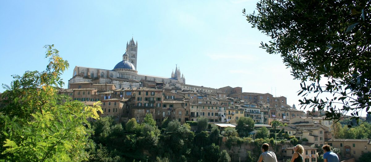 De skyline van Siena met de Dom, gezien tussen de bomen van een park · Italiaanse grammatica C1