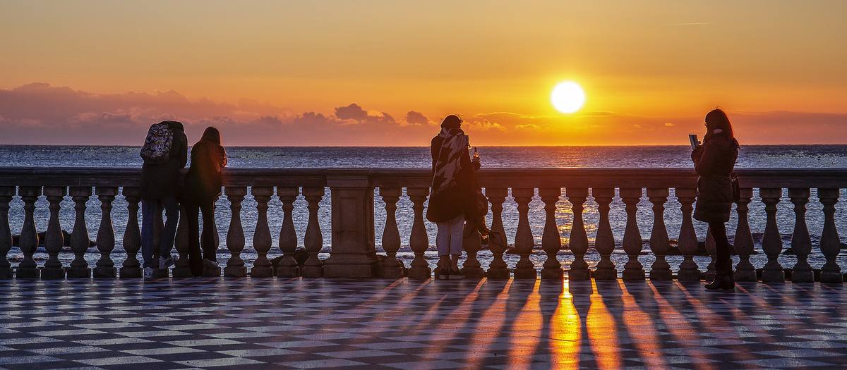 リヴォルノのマスカーニ・テラスの欄干で海に沈む夕日を見る人々