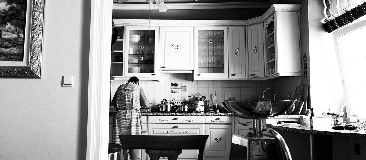 Een vrouw die kookt op het fornuis in een huiskeuken, in zwart-wit