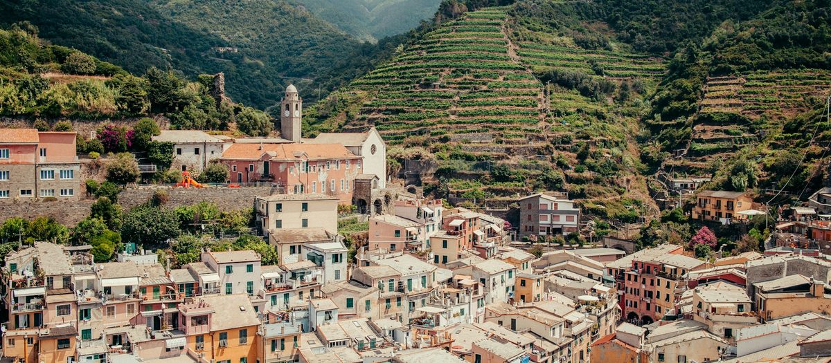 Een dorp met gekleurde huizen onder wijngaarden op terrassen · Italiaanse grammatica A2