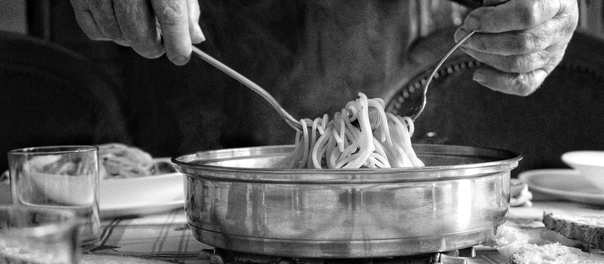 Twee handen die spaghetti uit een pan opscheppen