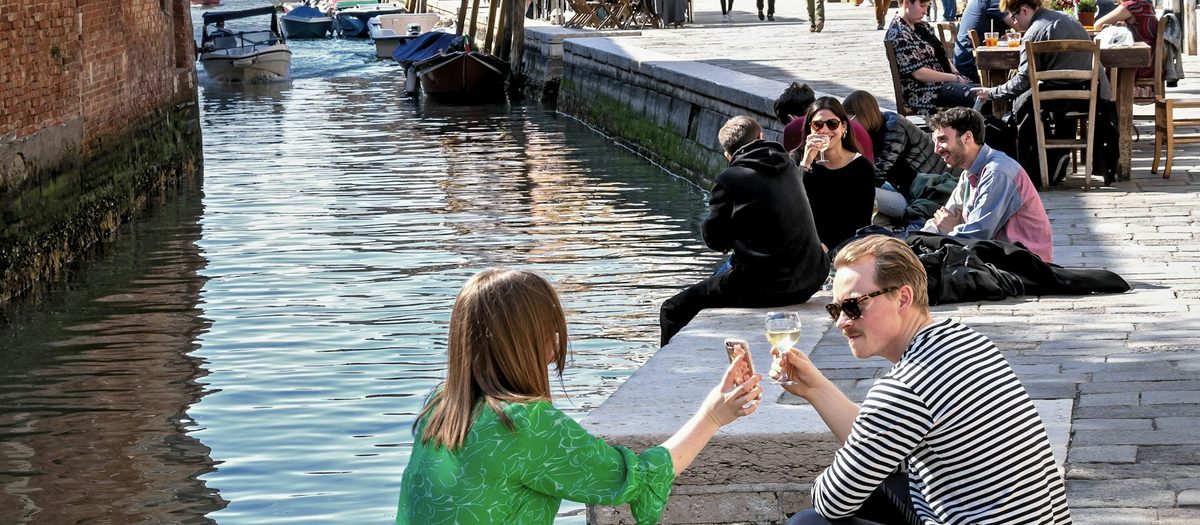 Mensen aan de rand van een Venetiaanse gracht, met glazen in de hand · Italiaanse grammatica A2