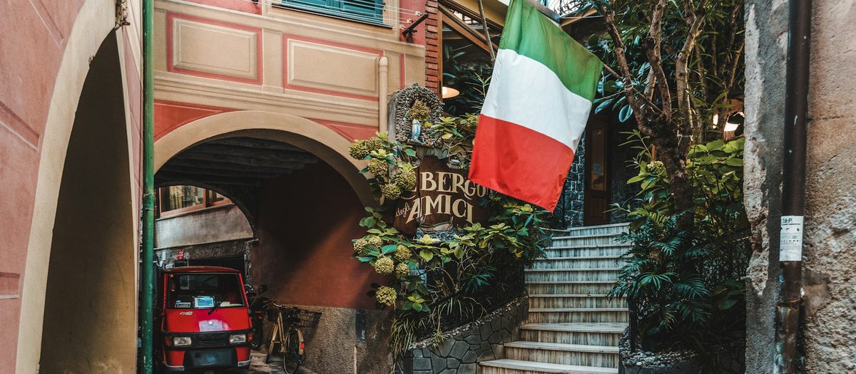 Een steil steegje, met de boog, de vlag en het bord van een hotel · Italiaanse grammatica A1