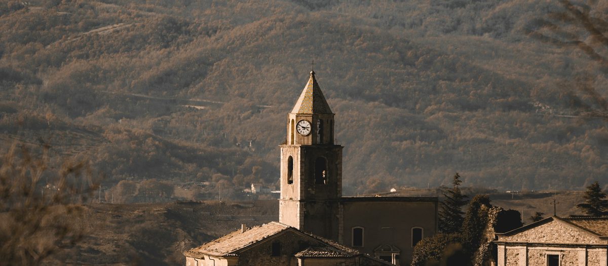Une église de village avec son clocher et son horloge, à flanc de montagne · grammaire italienne B1