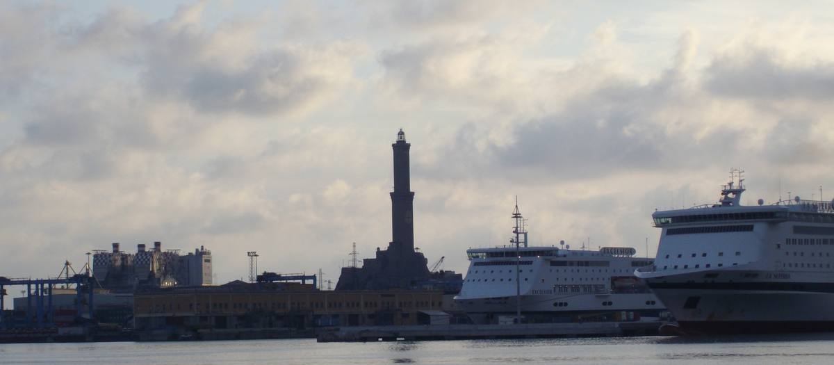 Der Hafen von Genua mit dem Leuchtturm Lanterna und zwei großen Fähren unter bewölktem Himmel
