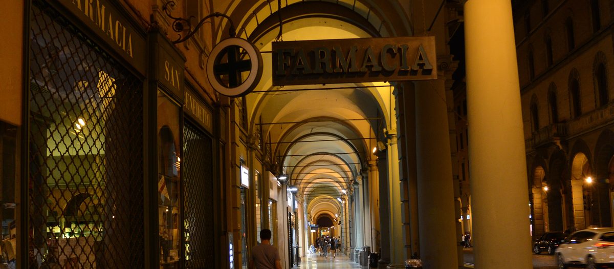 De zuilengangen van het Pavaglione in Bologna ’s avonds, met het apotheekbord