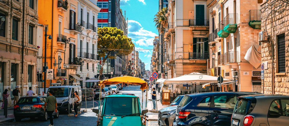 Een stadsstraat met auto’s, scooters en tafeltjes in de schaduw · Italiaanse grammatica A1