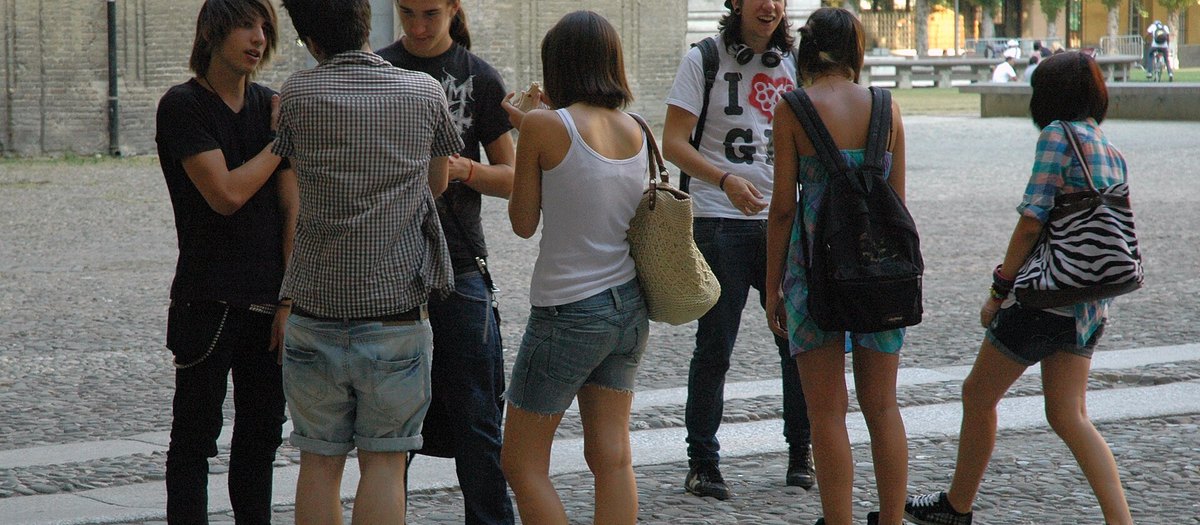 Një grup të rinjsh në këmbë duke folur, në një shesh · gramatika italiane A1