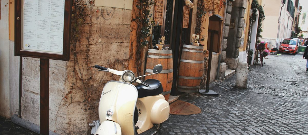 Een steegje met het menu aan de muur, twee vaten en een Vespa · Italiaanse grammatica B1
