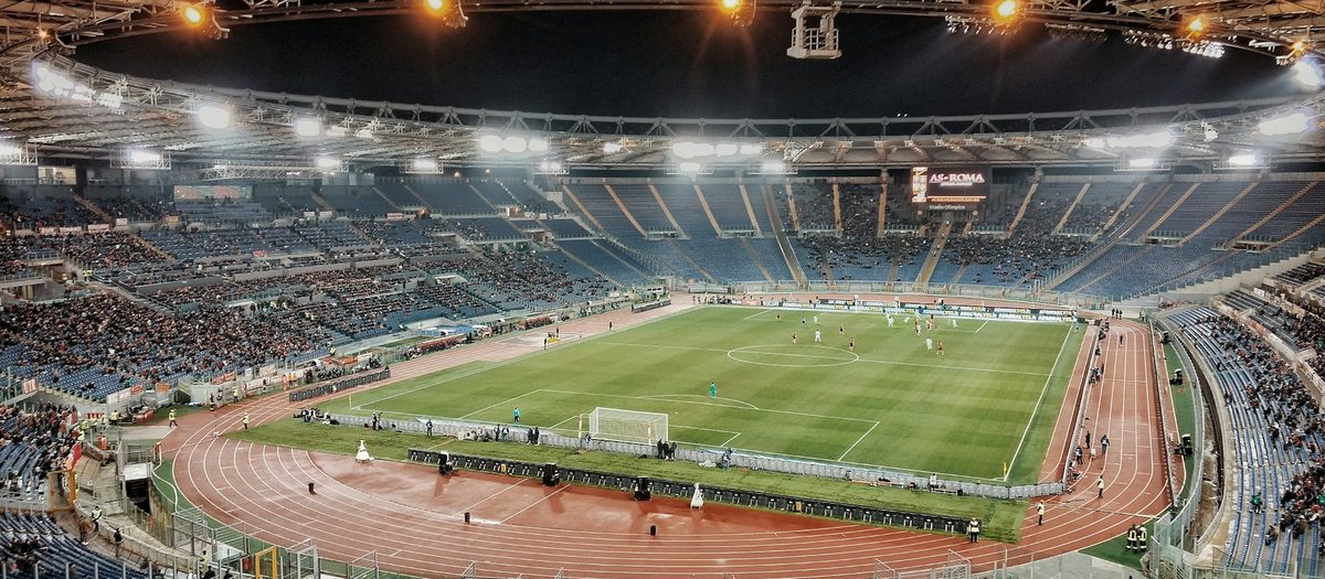 Een verlicht stadion van bovenaf, met de atletiekbaan om het veld · Italiaanse grammatica A2