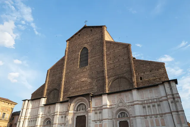 La facciata incompiuta in mattoni e marmo della Basilica di San Petronio a Bologna contro il cielo azzurro