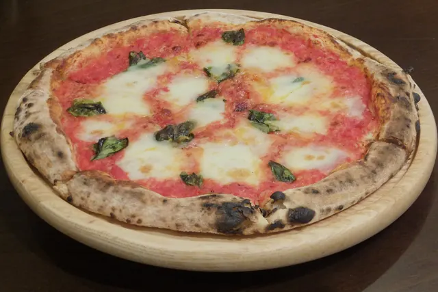 A Margherita pizza with tomato, mozzarella and basil on a round wooden board