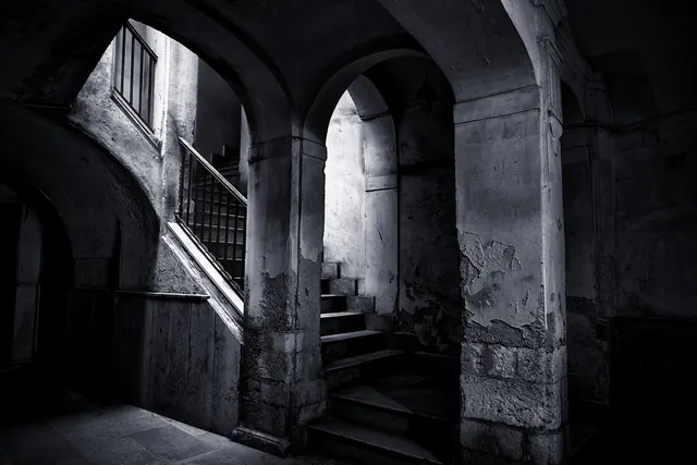 Archi di pietra e una scala nell'androne di un vecchio palazzo, in bianco e nero