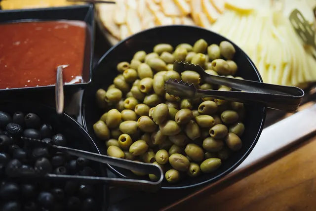 Bowls of green and black olives with serving tongs