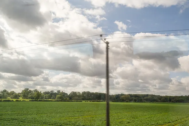 Green fields and a cloudy sky seen through a train window