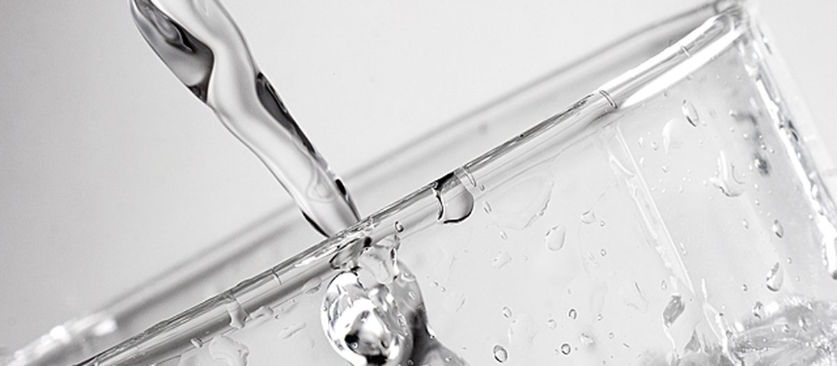 Un getto d’acqua che riempie un bicchiere di vetro, in primo piano.