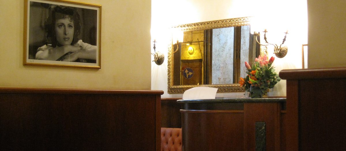 La reception di un albergo, con il bancone di legno, uno specchio dorato e un divano di pelle.