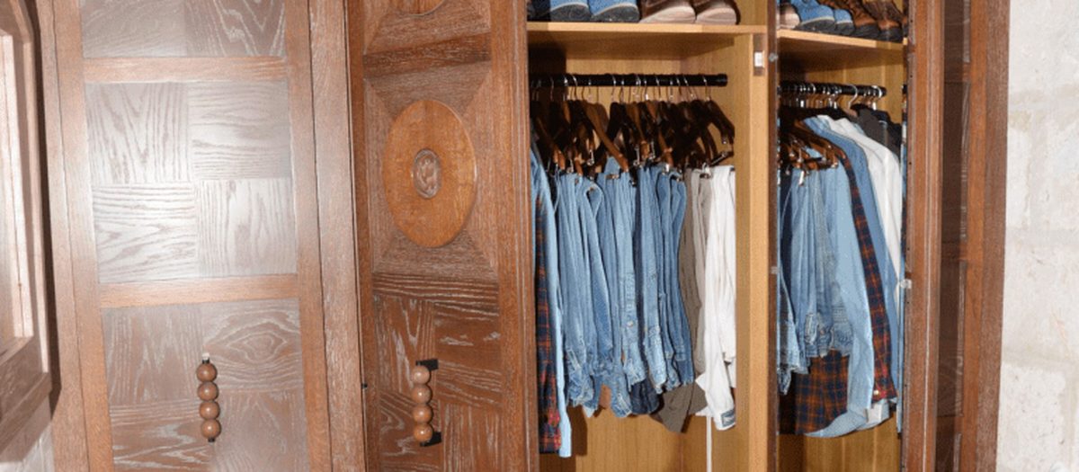 Un armadio di legno scuro aperto, con le camicie appese alle grucce e le scarpe sui ripiani.