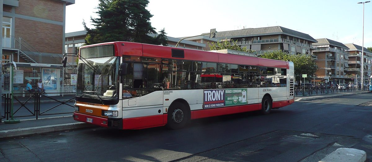 Un autobus urbano bianco e rosso fermo accanto alla pensilina, in una strada di Roma.