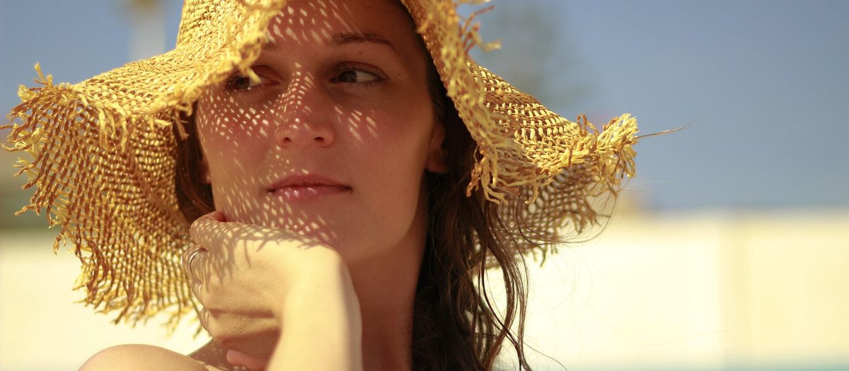 Una donna con un cappello di paglia a tesa larga, controluce, con l’ombra della trama sul viso.