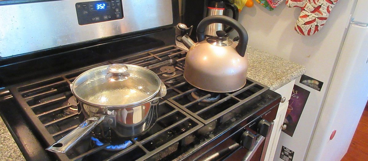 I fornelli di una cucina di casa, con una pentola sul fuoco, il bollitore e le presine appese al muro.