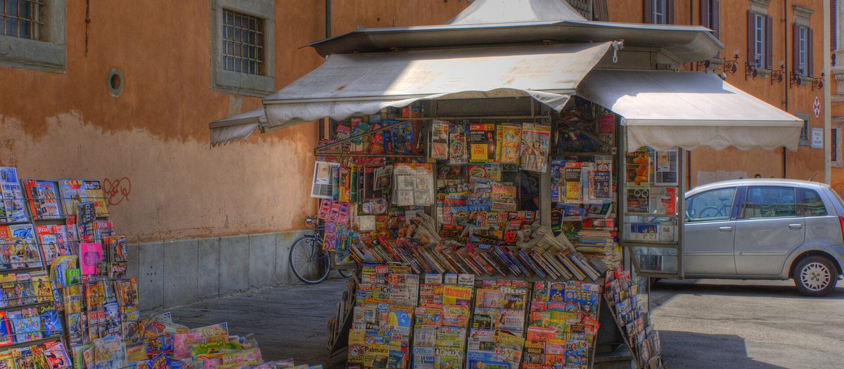 Un'edicola in una piazza, coperta di giornali e riviste esposti.