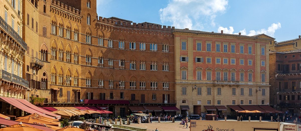Piazza del Campo a Siena, con i palazzi di mattoni e gli ombrelloni dei bar sotto i portici.