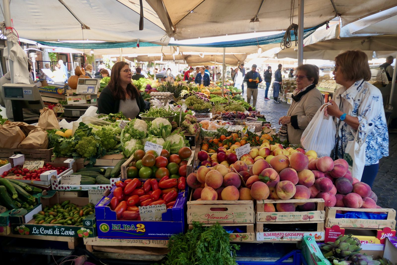Een groente- en fruitkraam op Campo de' Fiori in Rome, met kisten perziken en tomaten en klanten voor de toonbank
