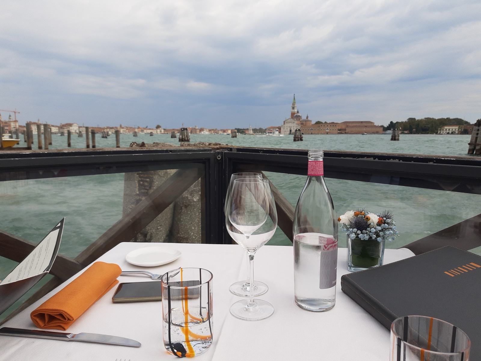 Gedekte tafel van een Venetiaans restaurant aan het water, met de menukaart en uitzicht op San Giorgio Maggiore