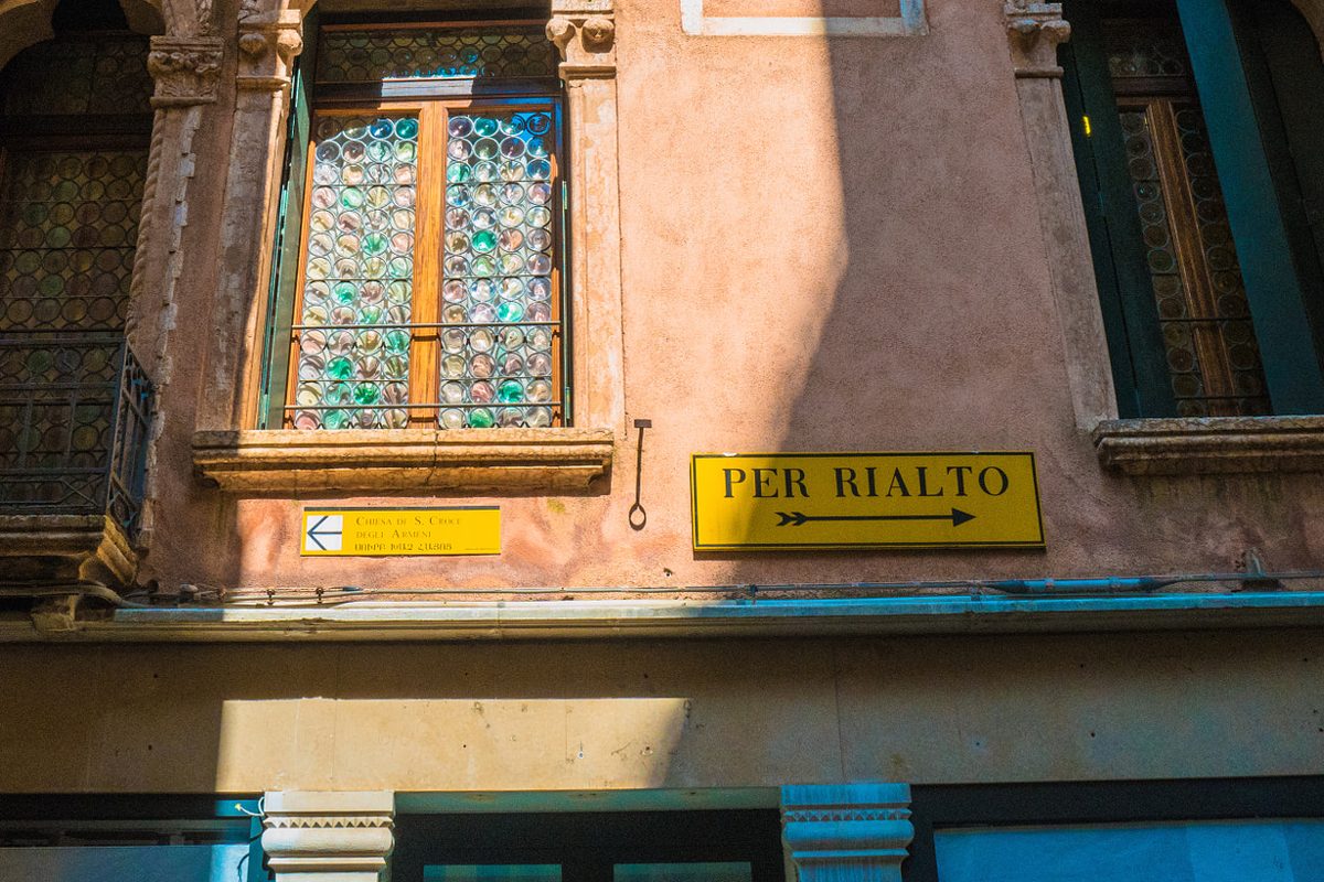 A yellow «Per Rialto» sign on a building in Venice