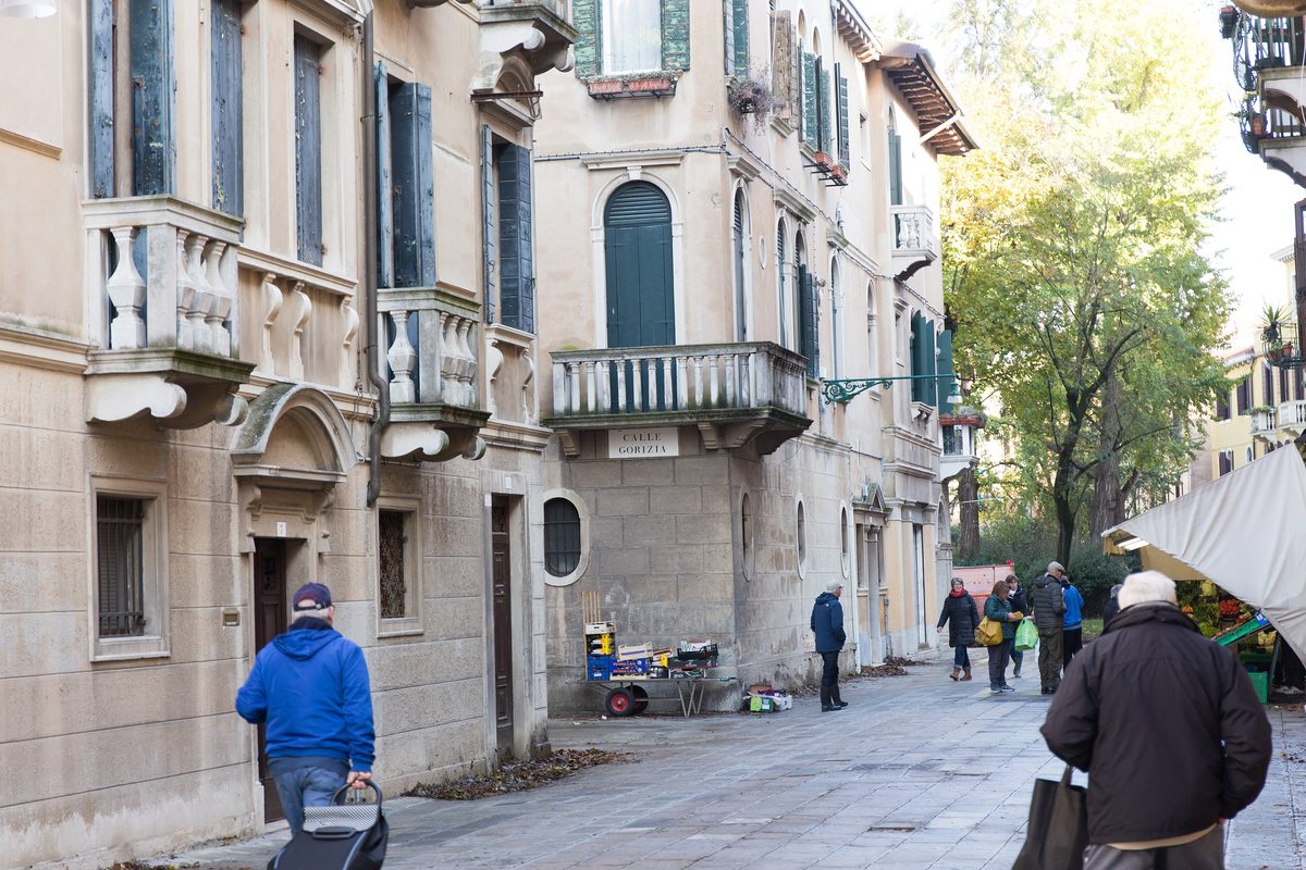 People walking along Calle Gorizia in Venice, between old houses with shutters