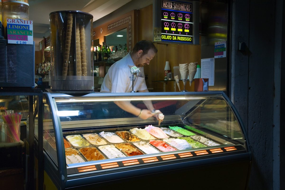 A server behind the glass display of gelato tubs in a gelateria in Venice