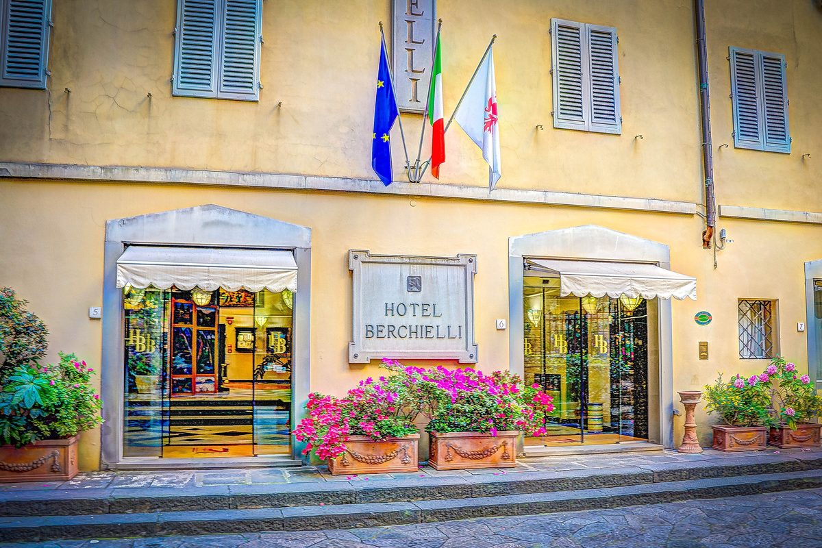 Entrance of a small hotel in Florence with flags, flowers and an awning