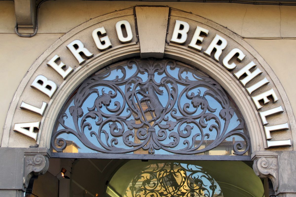 A wrought-iron arch with the name «Albergo Berchielli» over a hotel entrance on the Lungarno in Florence