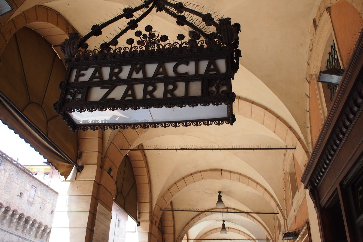 The wrought-iron sign of the Farmacia Zarri under the arcades of Via Ugo Bassi, Bologna
