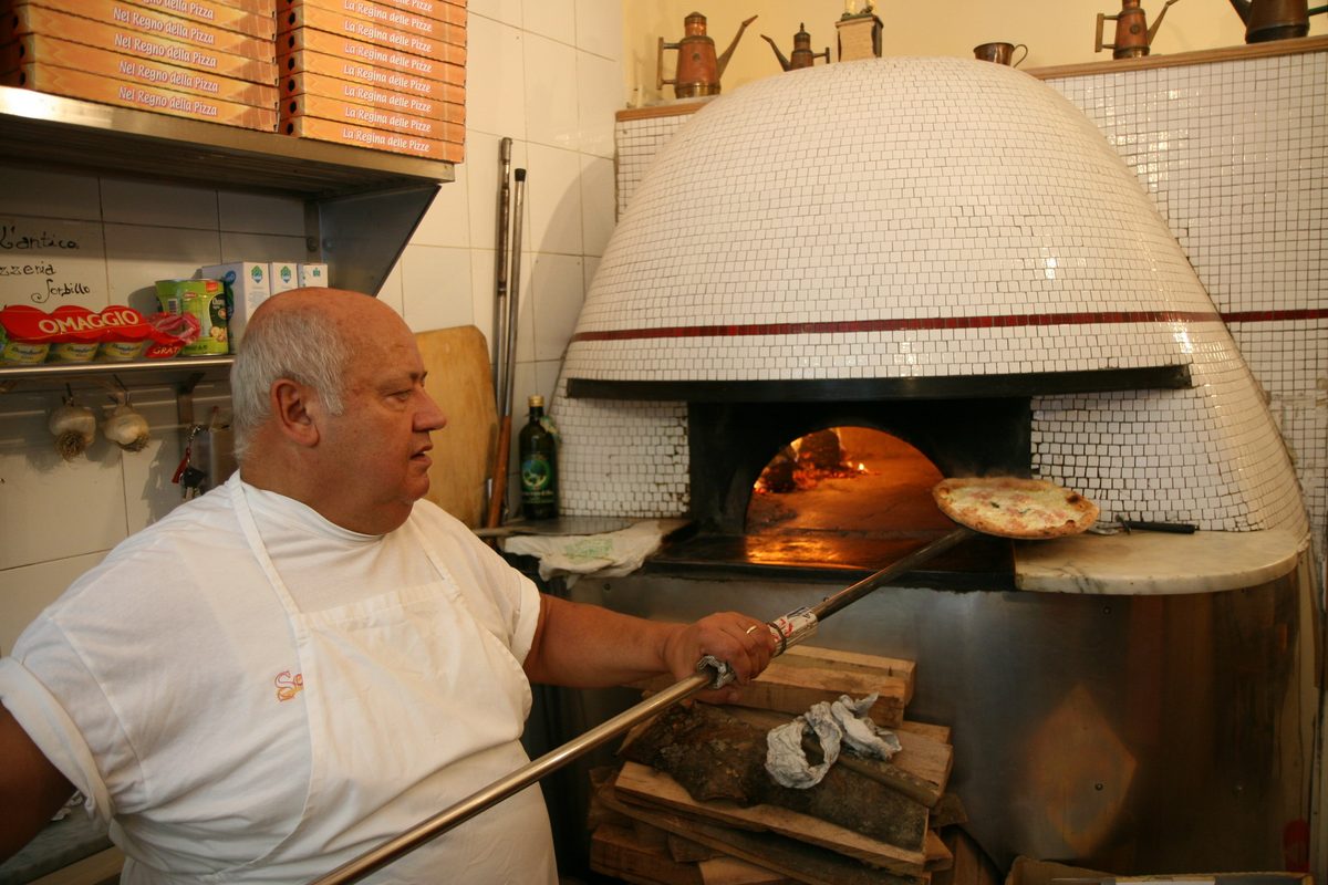 A pizzaiolo putting a pizza into a wood-fired oven in Naples