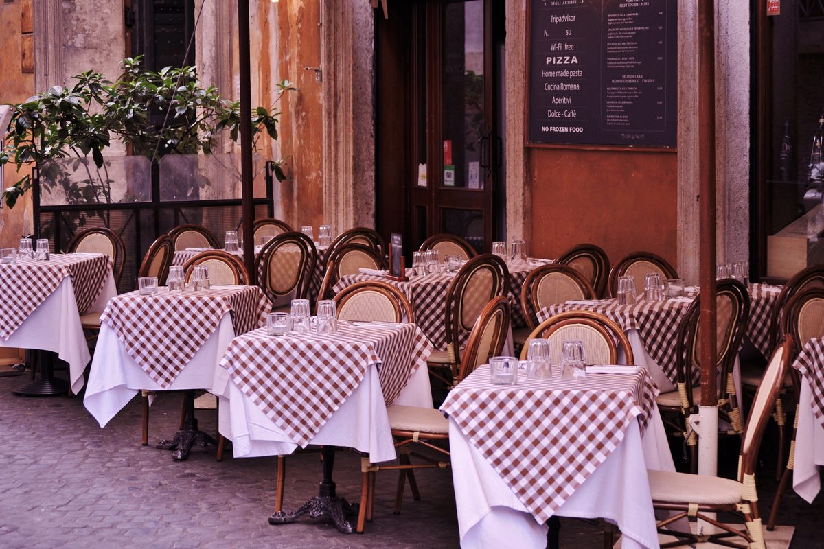 Restaurant tables with red checked tablecloths and the menu on a chalkboard, in an Italian street