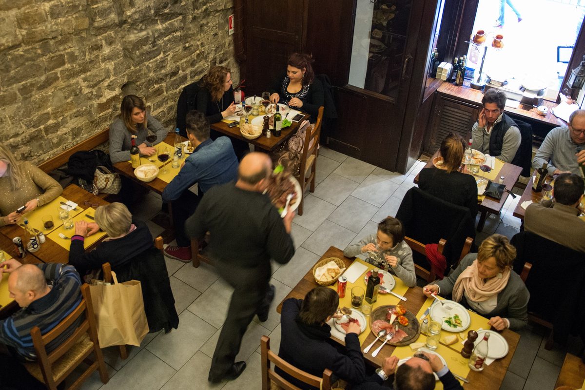 A waiter carrying plates between busy tables in a Florentine osteria