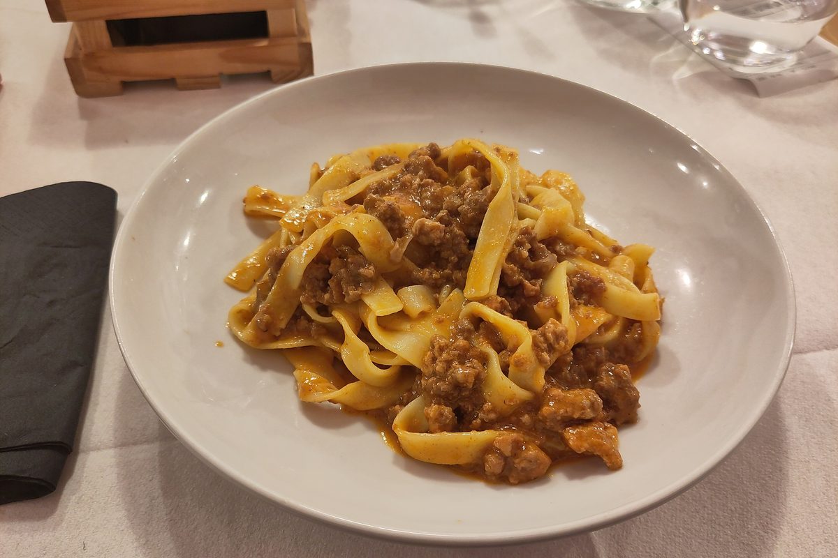 A plate of tagliatelle al ragù on a white tablecloth in a Bologna trattoria
