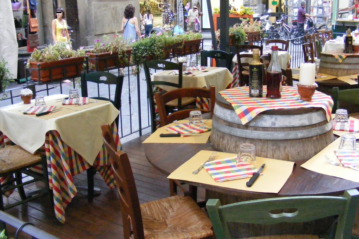 Outdoor restaurant tables with striped tablecloths and an old wine barrel used as a table in Florence