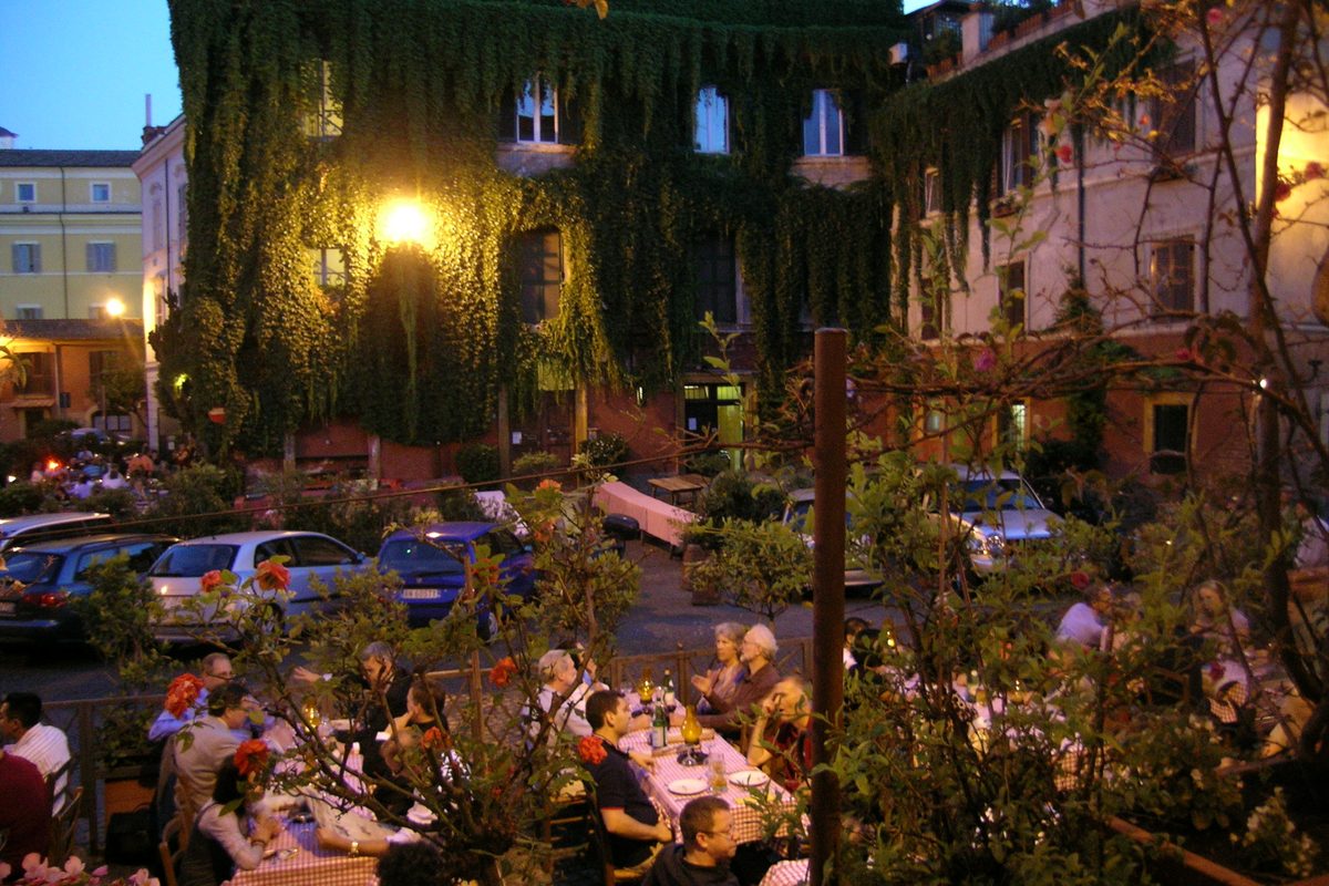 Diners at the tables of a busy open-air restaurant in Trastevere, Rome, in the evening