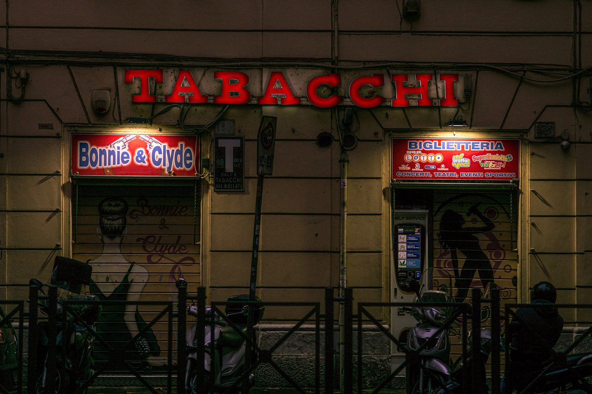 The red neon sign of a tabaccheria in Rome at night, with the T sign by the door