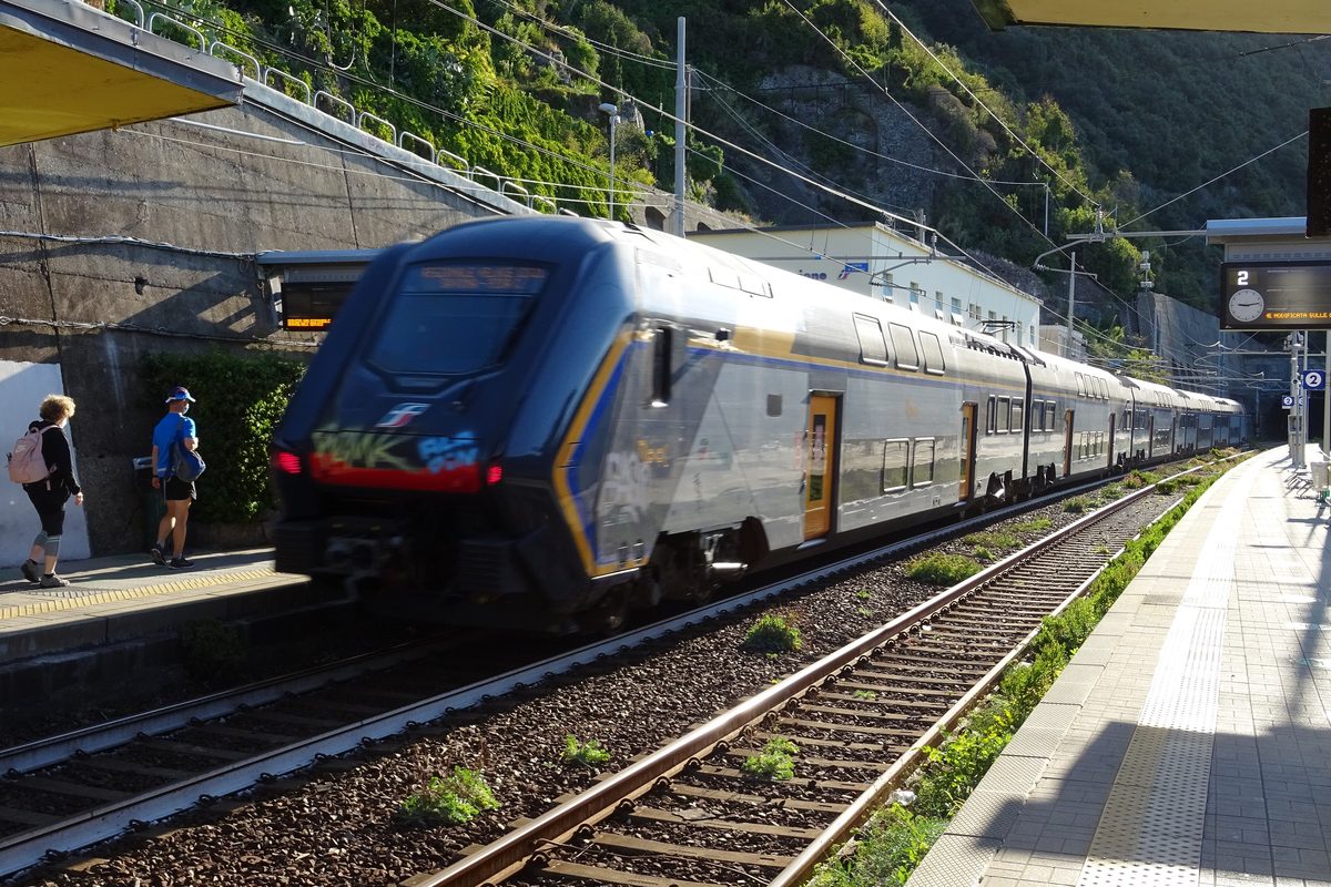 A blue and white regional train passing through Corniglia station in the Cinque Terre