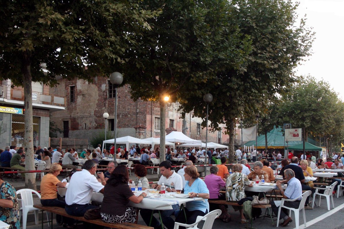 Long tables full of people eating outdoors under the trees at the chicken festival in Airasca