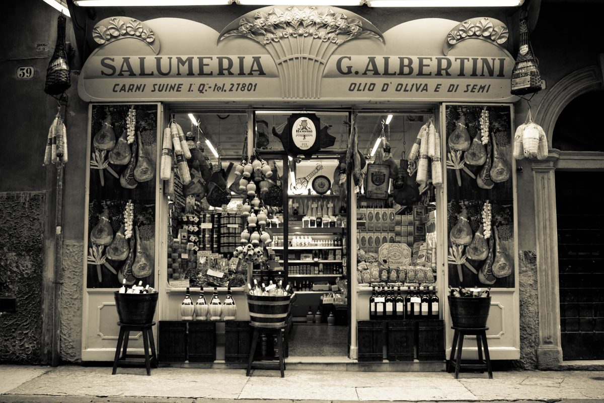 The window of an old-fashioned salumeria, «Salumeria G. Albertini», with hams hanging inside