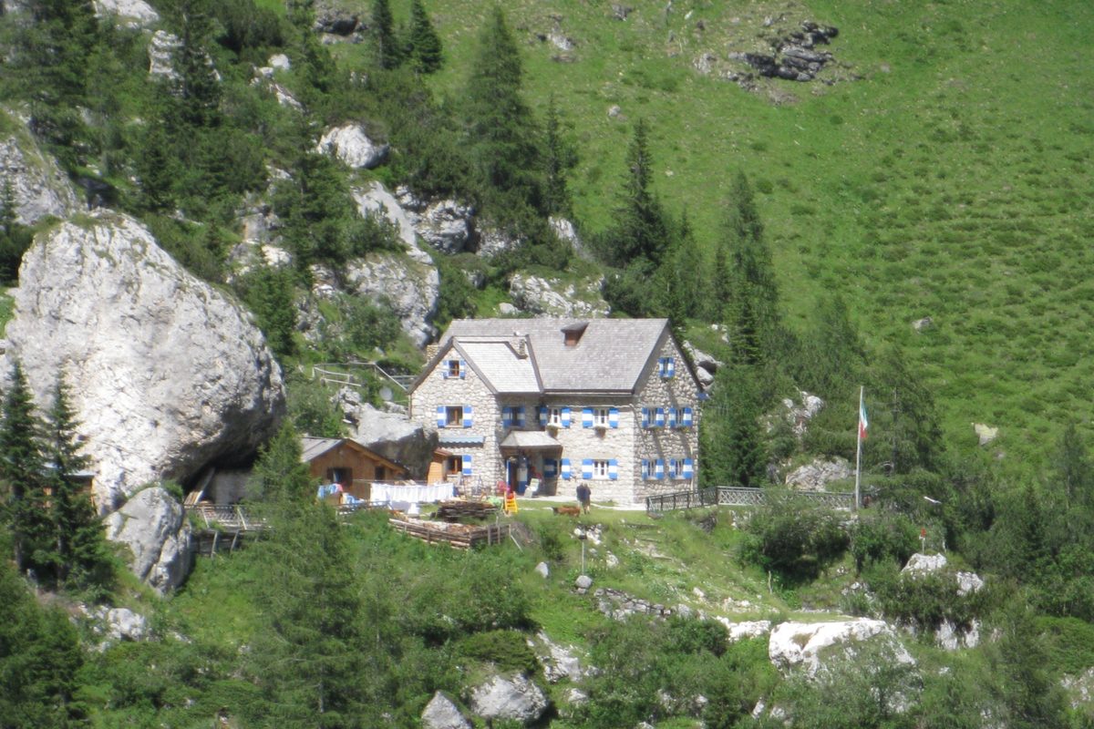 The white Rifugio Falier in a green valley below the Marmolada cliffs