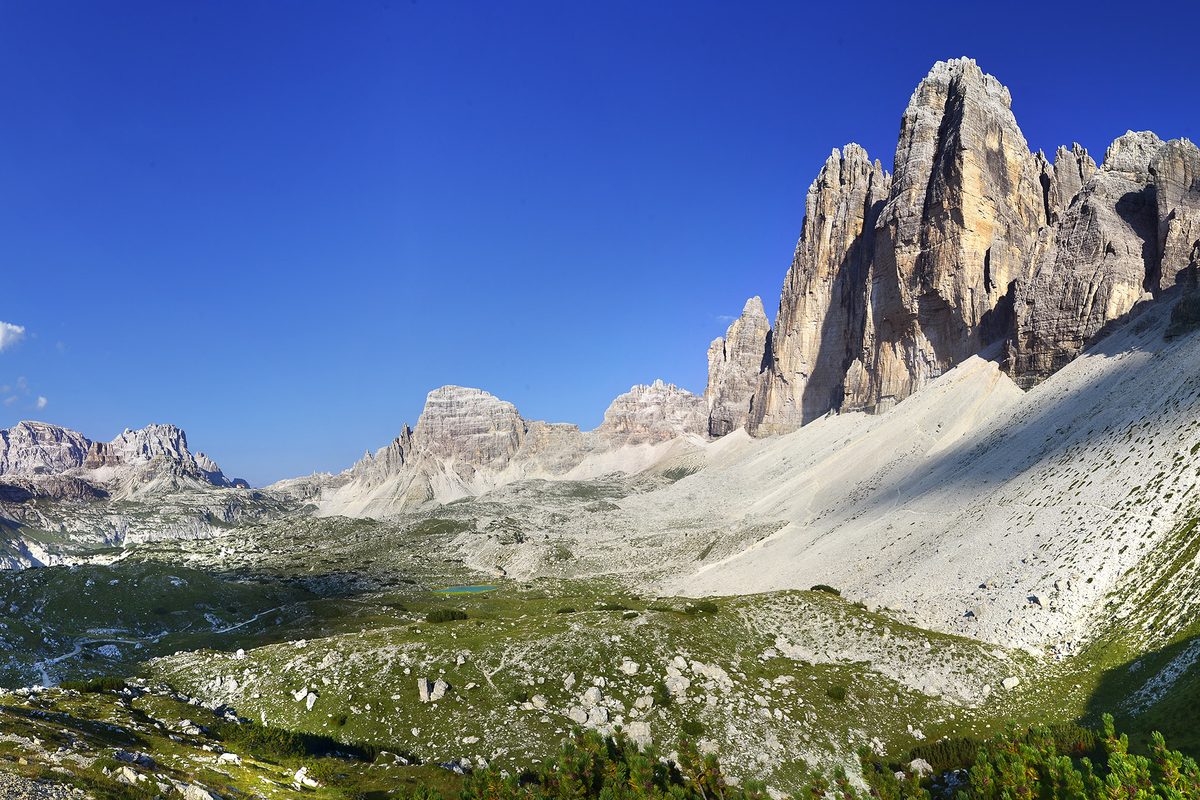 The Tre Cime di Lavaredo above a wide valley, with a mountain hut in the distance