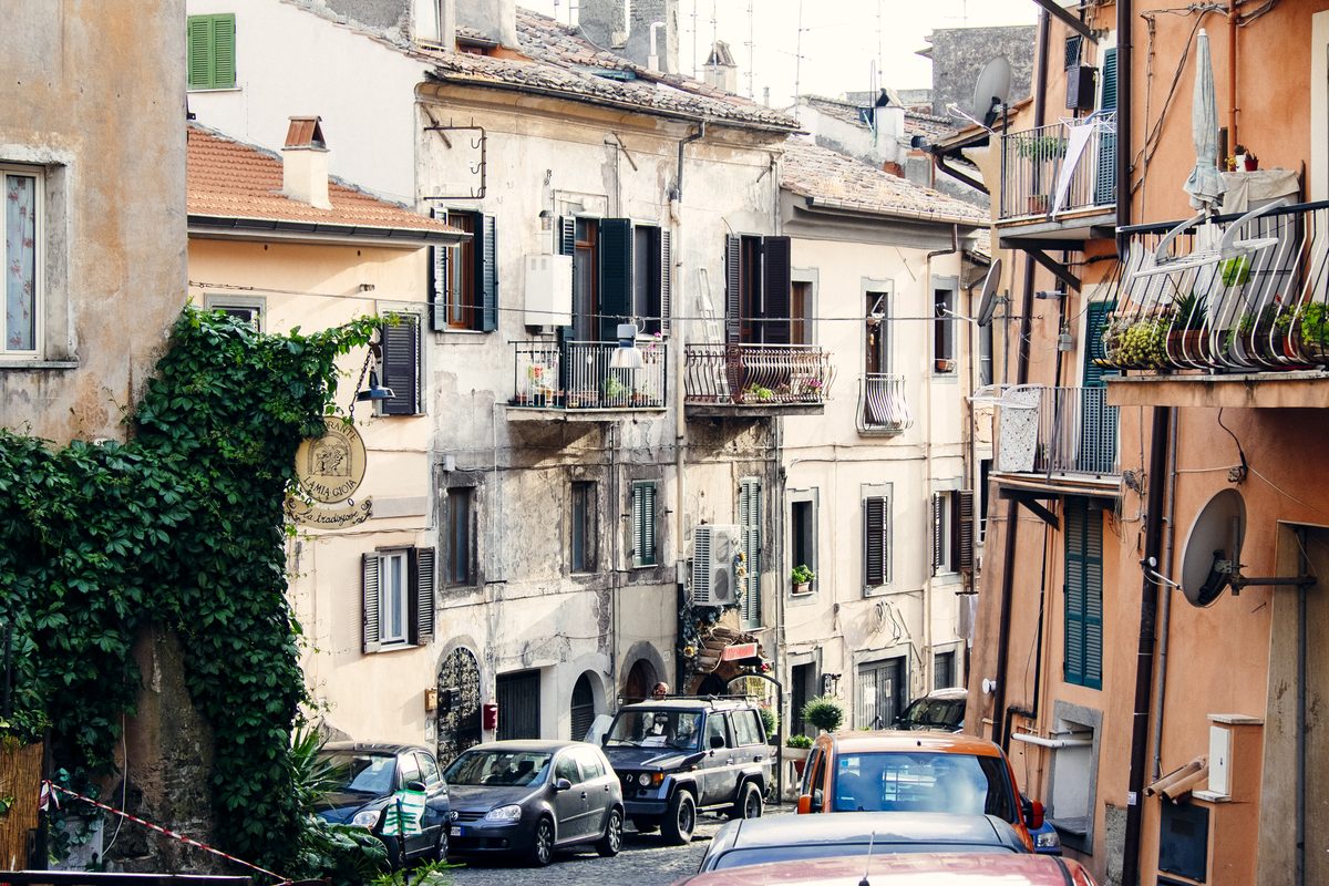 A steep street of tall houses with small balconies and parked cars in Genzano di Roma